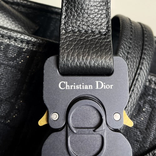 Close-up of the buckle on the CHRISTIAN DIOR KIM JONES BLACK OBLIQUE MONOGRAM TOTE BAG showing the Christian Dior logo.