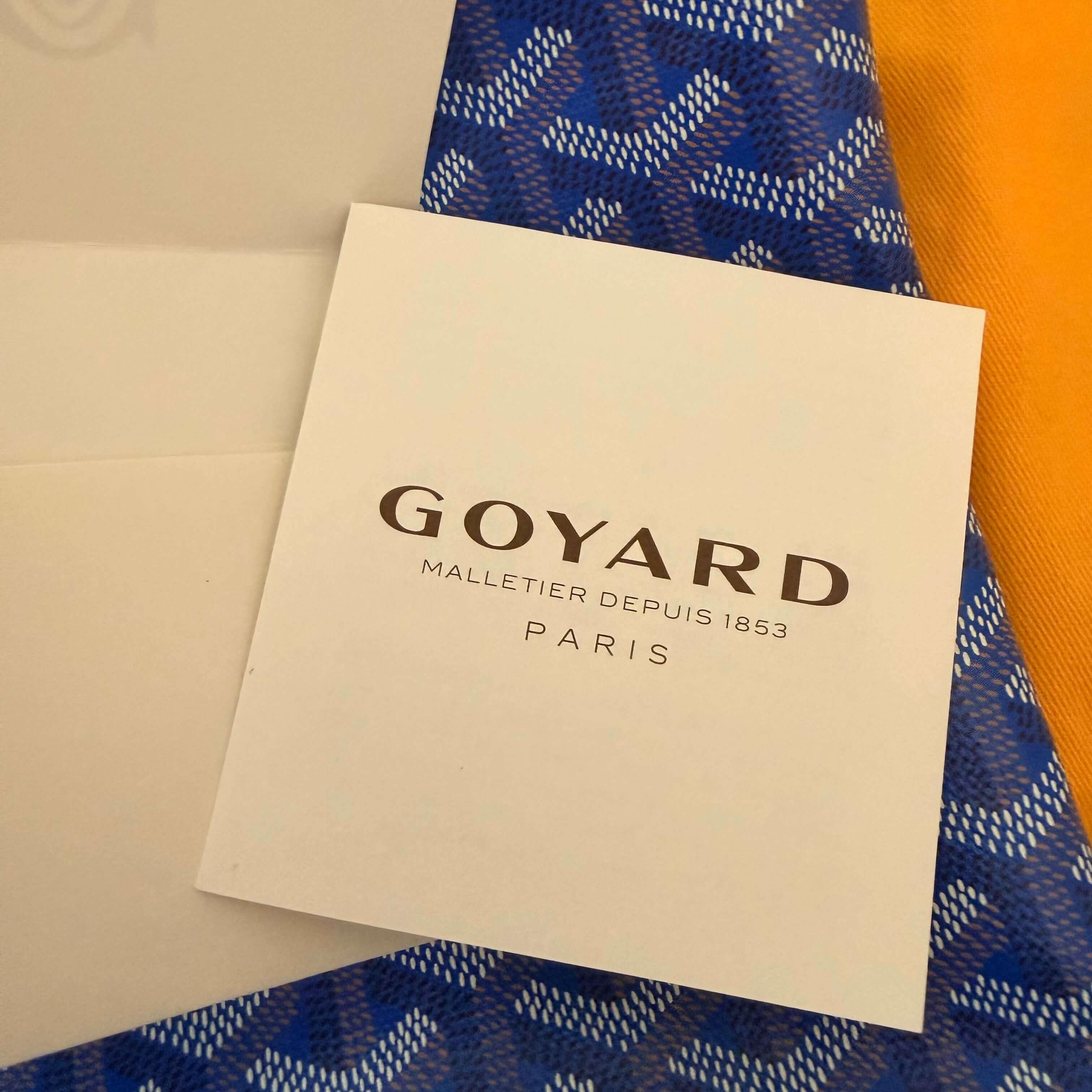 Goyard Artois MM Tote Bag- Goyardine care card with Goyard branding in blue pattern background.
