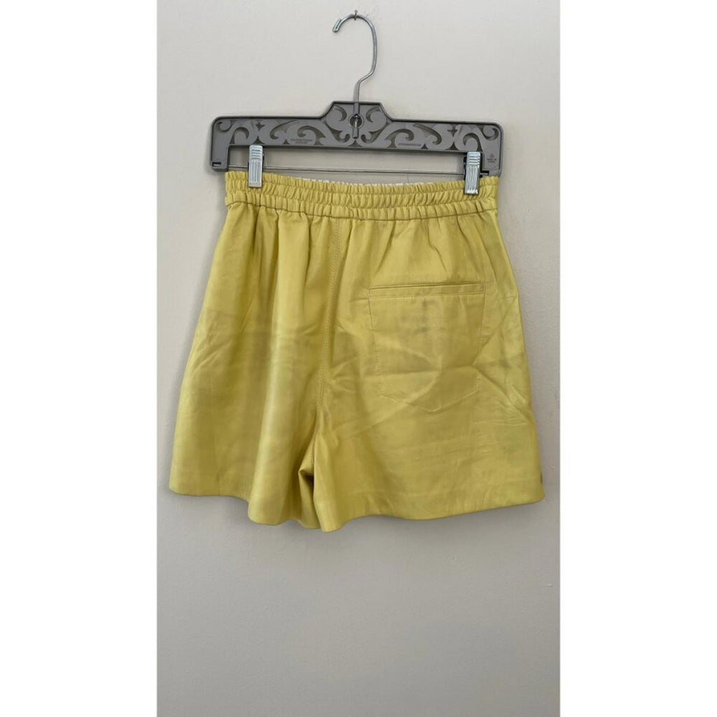 NANUSHKA YELLOW VEGAN LEATHER ELASTIC WAIST SHORTS displayed on a hanger, showcasing the back view and pocket.