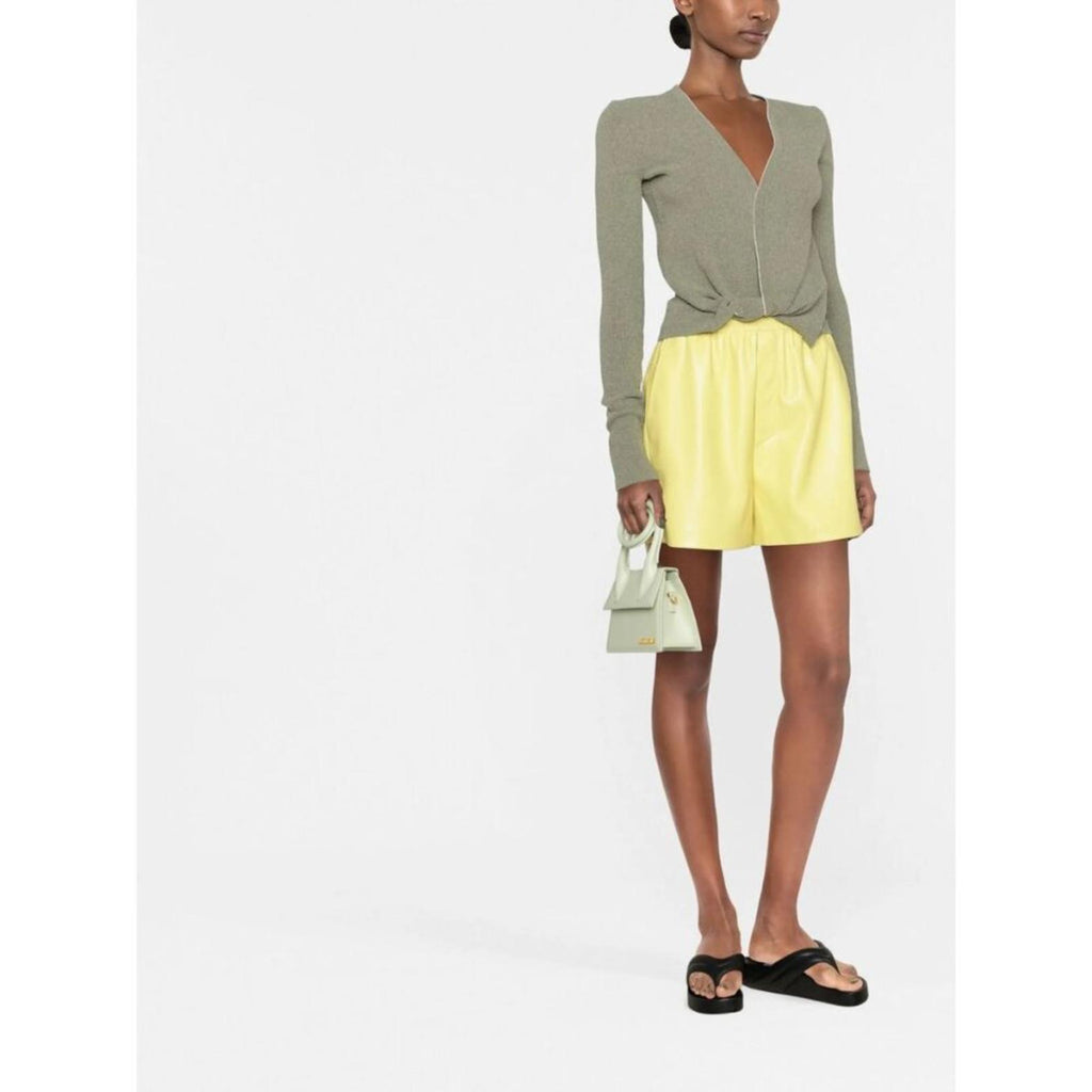 Model wearing NANUSHKA YELLOW VEGAN LEATHER ELASTIC WAIST SHORTS styled with a green top and small handbag.